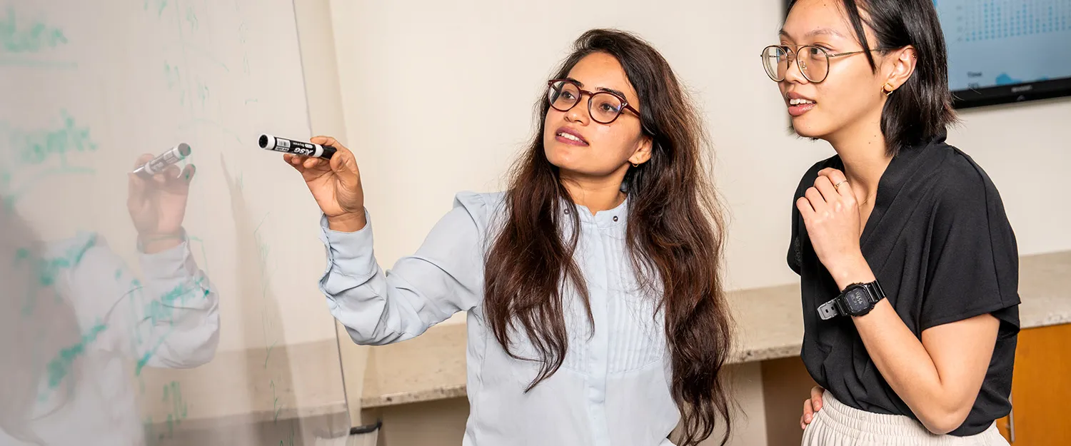 Two students work together at a white board during an economics class.