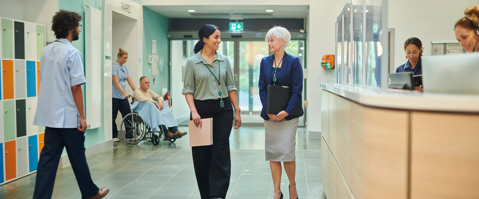 Hospital employees discuss health management issues while walking down a hallway.