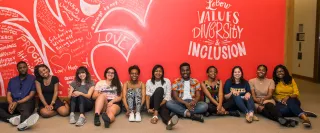 Eleven smiling students sitting in front of a red wall that reads "LeBow values diversity & inclusion"