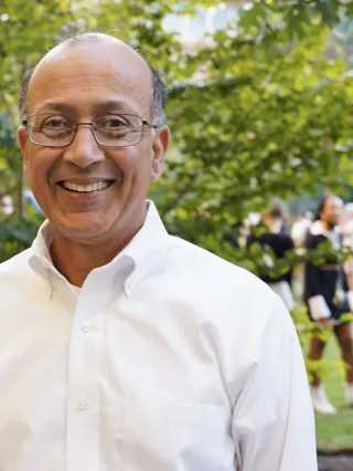 Dean Madan in white shirt standing on Drexel's campus with people in the background.